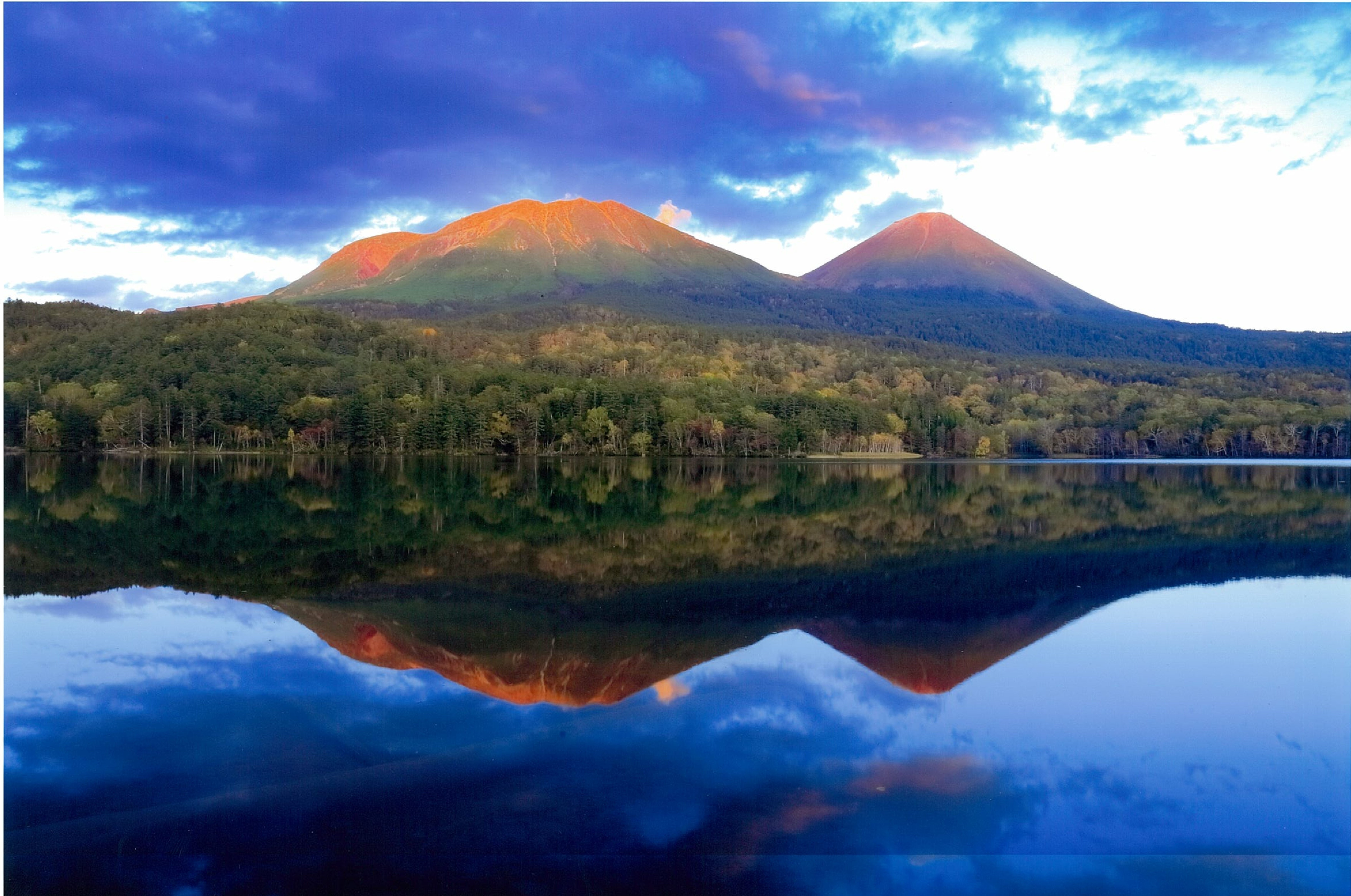風のないオンネトーの夕景、夕陽が照らす雌阿寒岳と阿寒富士の神々しい姿を澄み切った湖面が映し出している。